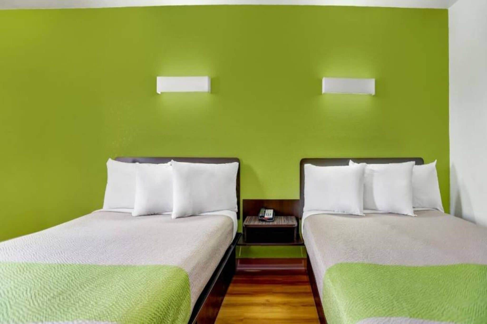 Hotellihuone, jossa on kaksi erillistä sänkyä, puulattia ja vihreä seinä.