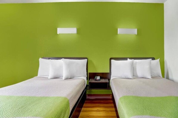A hotel room with two single beds, a wooden floor, and a green wall.