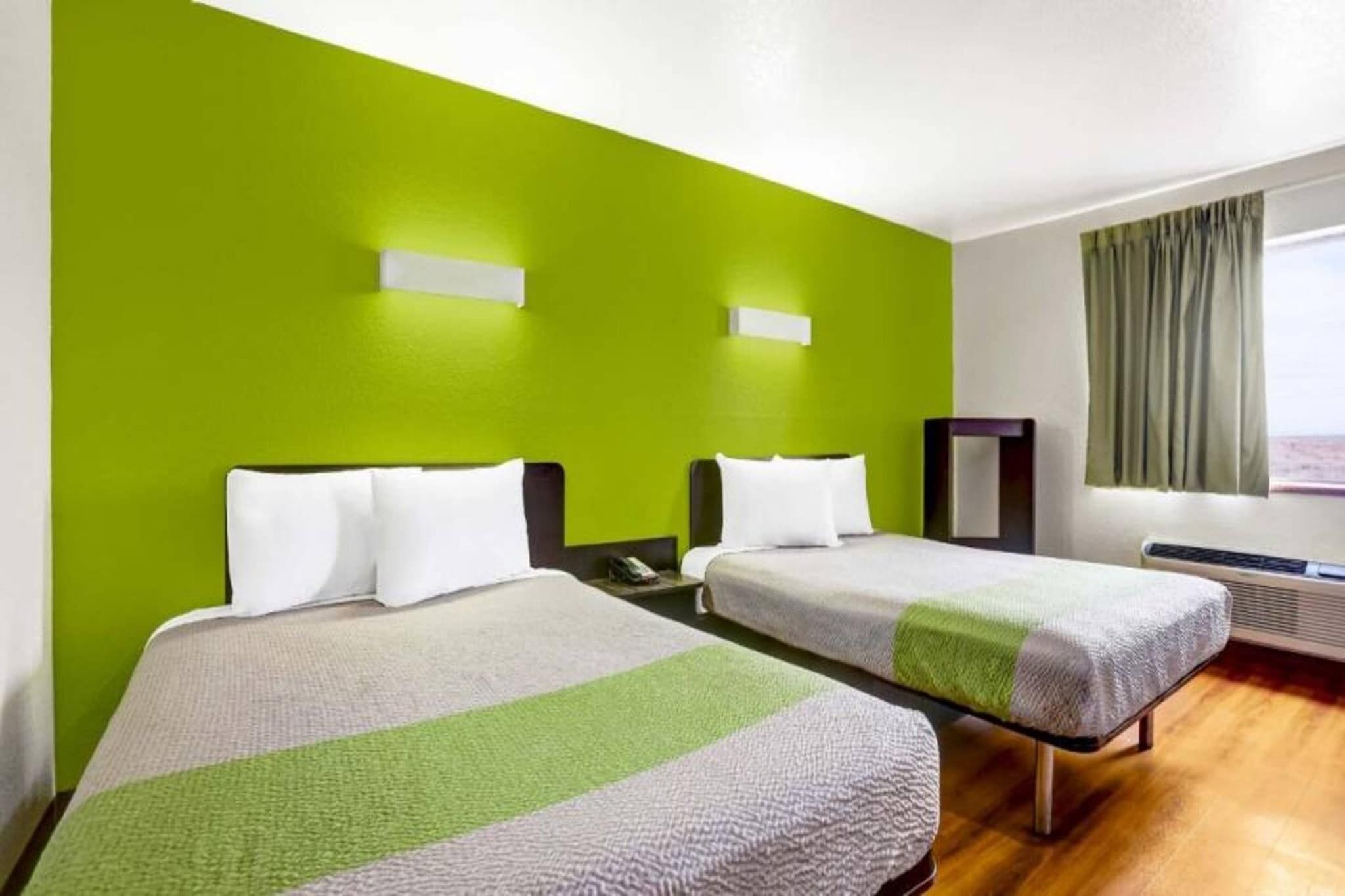 A hotel room with two beds, a large window with curtains, and a heater.
