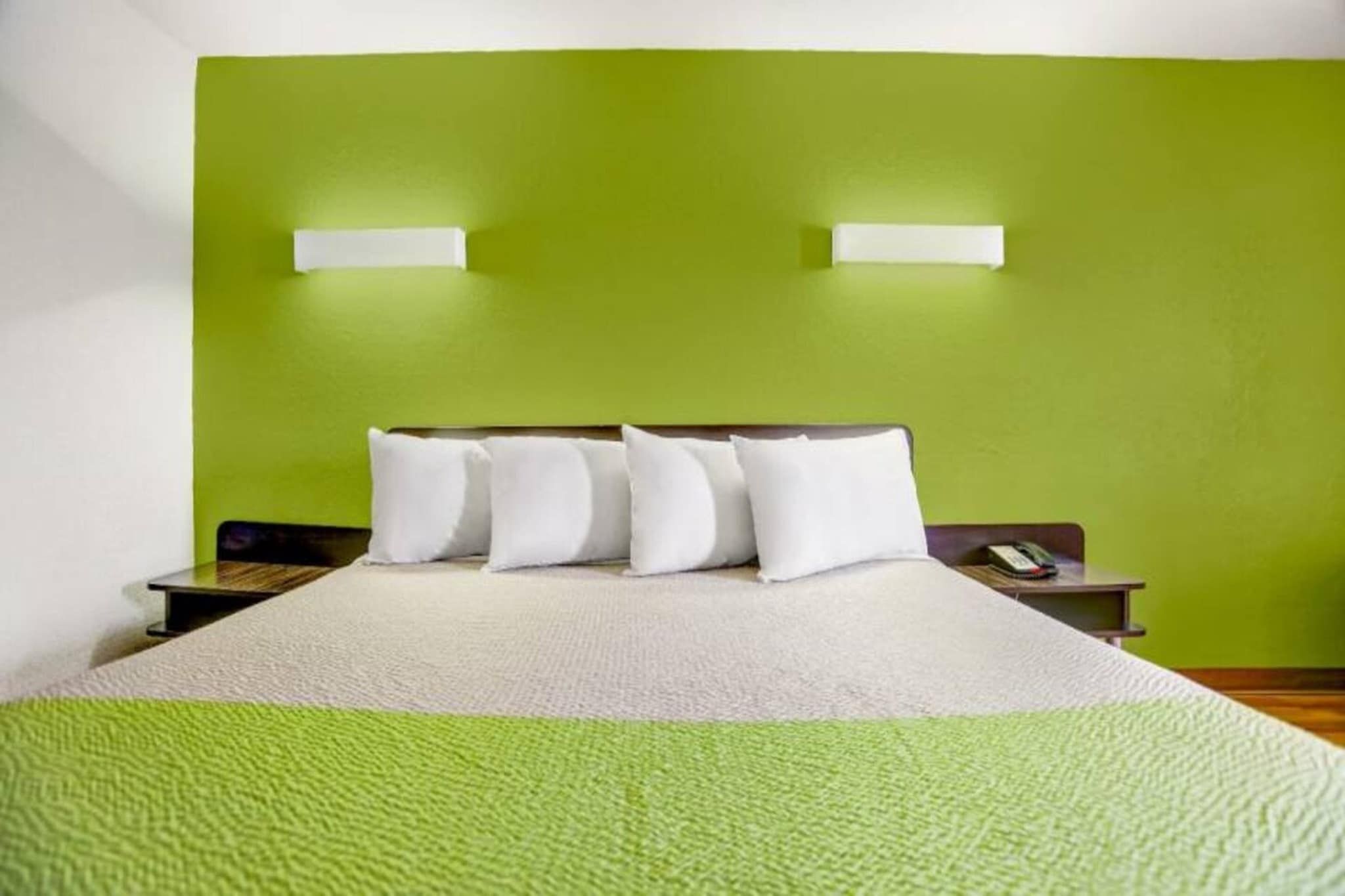Una habitación de hotel con una pared verde, una cama con ropa de cama blanca y dos mesitas de noche.
