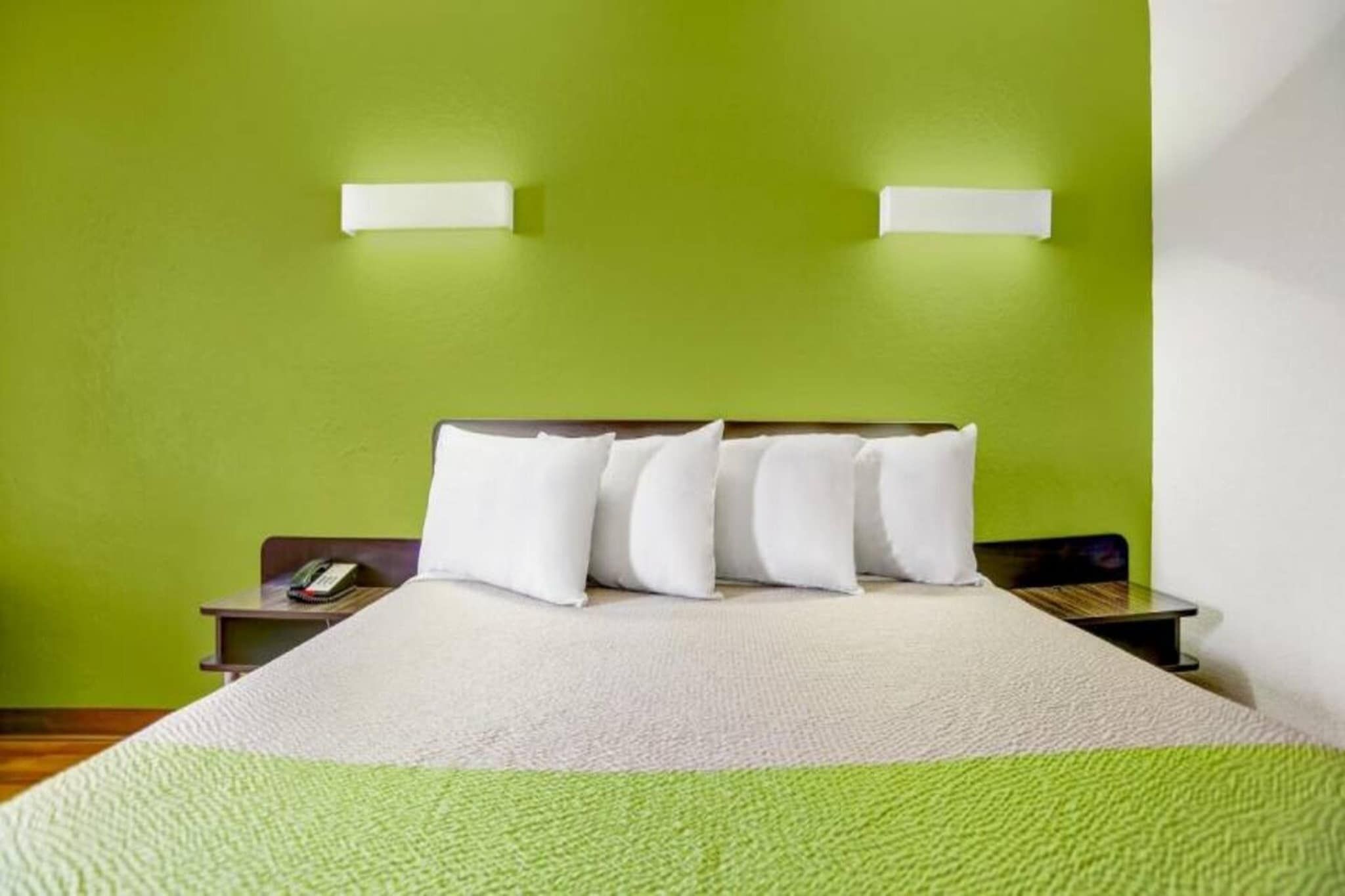 Hotellihuone, jossa on sänky, vihreät seinät, kaksi yöpöytää ja puhelin toisella yöpöydällä.