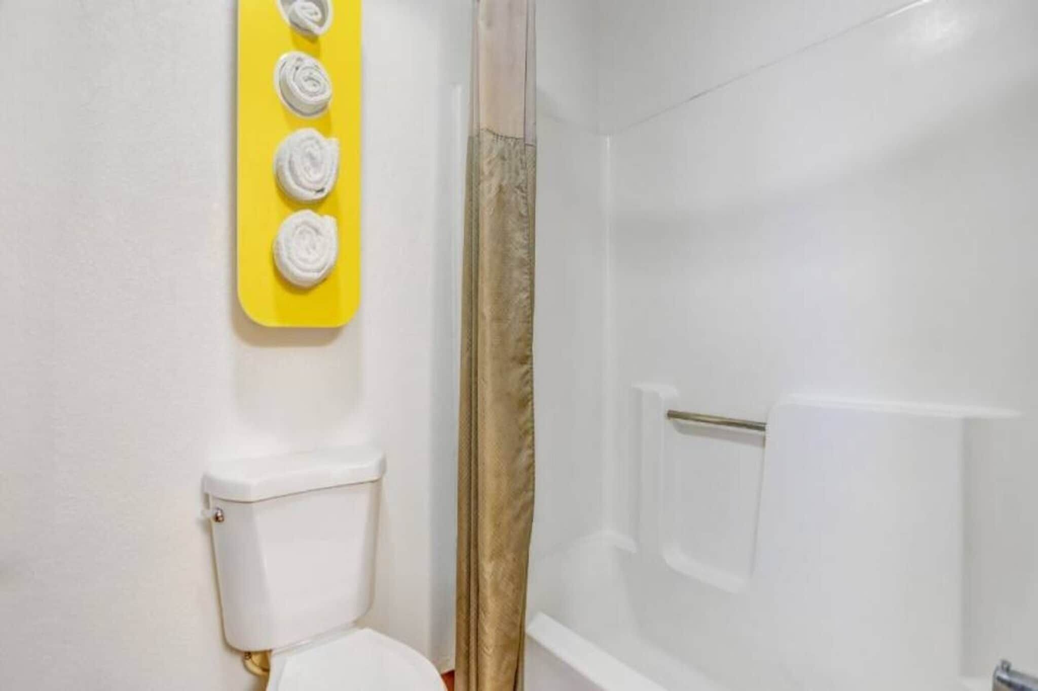 A bathroom with a toilet, a shower, and a yellow towel rack with four towels.
