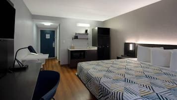Quarto de hotel com cama, escrivaninha, cadeira, cozinha compacta e televisão.