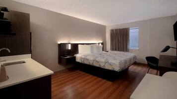 Een moderne hotelkamer met een houten vloer, een groot bed met beddengoed met een patroon, een nachtkastje met een lamp, een bureau met een stoel en een raam met gordijnen.