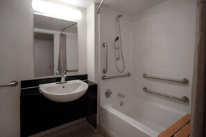 Een badkamer met een wastafel, spiegel, douche en handgrepen.