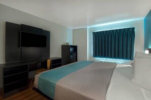Une chambre moderne avec un grand lit, un téléviseur à écran plat fixé au mur, une petite armoire et une fenêtre avec des rideaux.