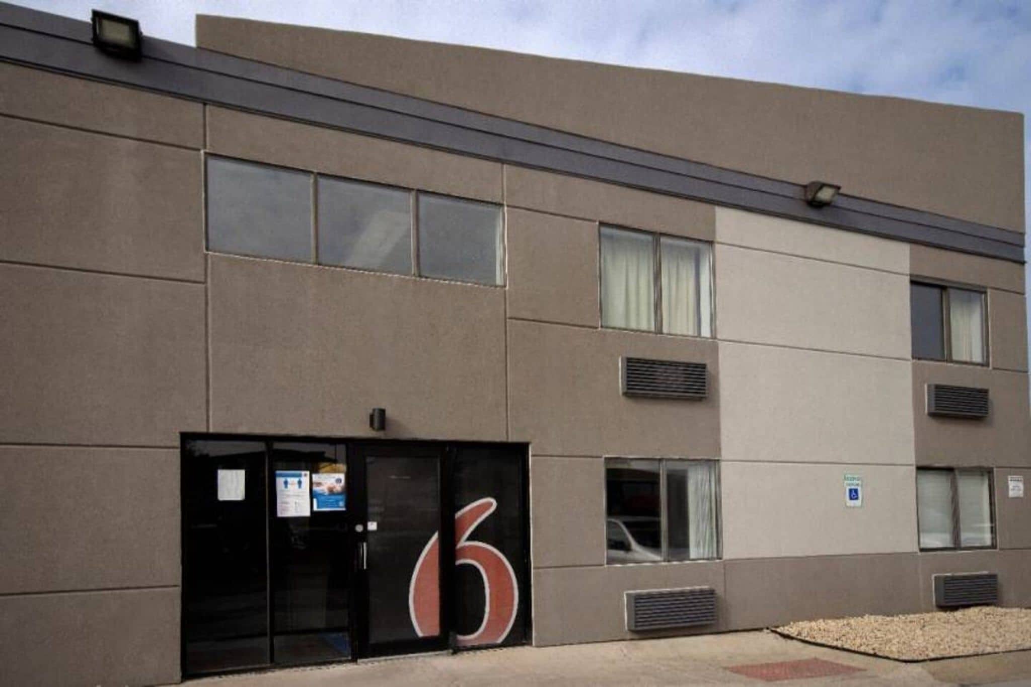 A modern building with a large number '6' sign, multiple windows, and air conditioning units.
