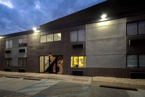 Un bâtiment moderne à la façade plate, doté de grandes fenêtres et d’un parking avec des places délimitées.