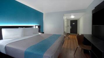 A hotel room with a large bed, a desk, a chair, and a television.