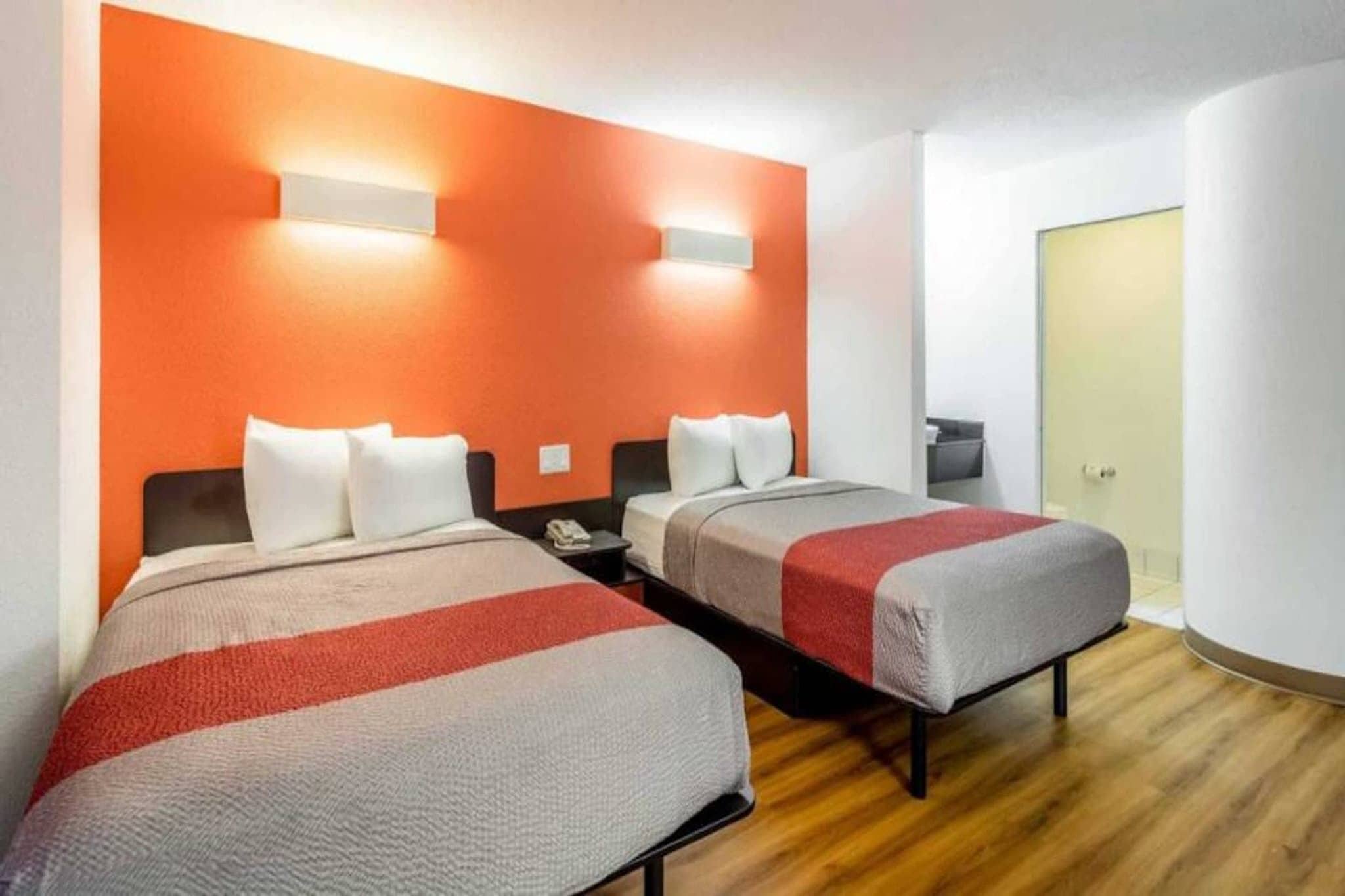 Quarto de hotel com duas camas, piso de madeira e uma porta ao fundo.