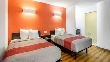 Quarto de hotel com duas camas, piso de madeira e uma porta ao fundo.