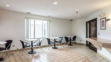 Quarto com piso em azulejos, uma janela grande e um espaço de estar com mesas e cadeiras.