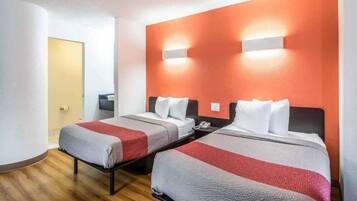 A hotel room with two beds, a wooden floor, and a red accent wall.
