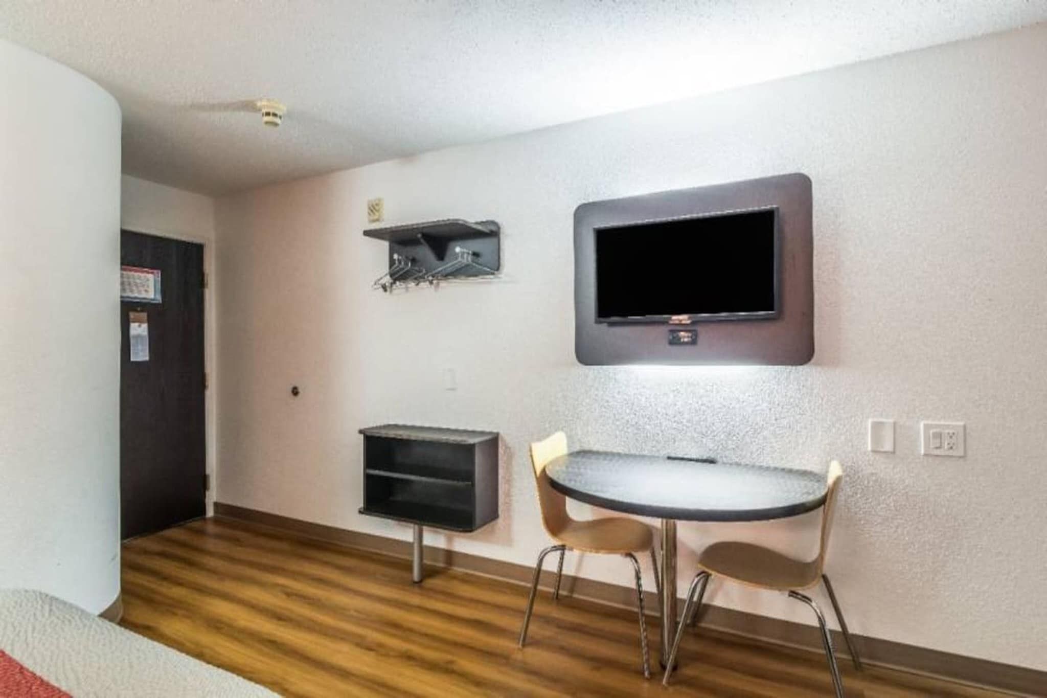 A small room with a flat-screen TV mounted on the wall, a small table with two chairs, and a wooden floor.
