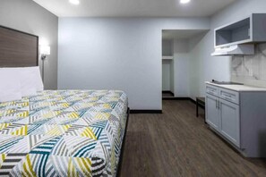 Une chambre d’hôtel avec un lit, une kitchenette et une salle de bain, visibles à travers une porte ouverte.