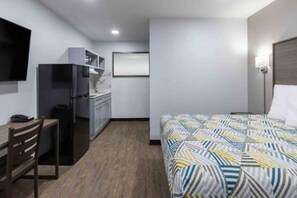 A hotel room with a bed, a desk, a chair, a kitchenette, and a television.