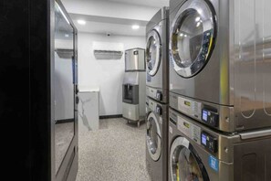 Een wasserette met gestapelde wasmachines en drogers, een waterdispenser en een kleine koelkast.