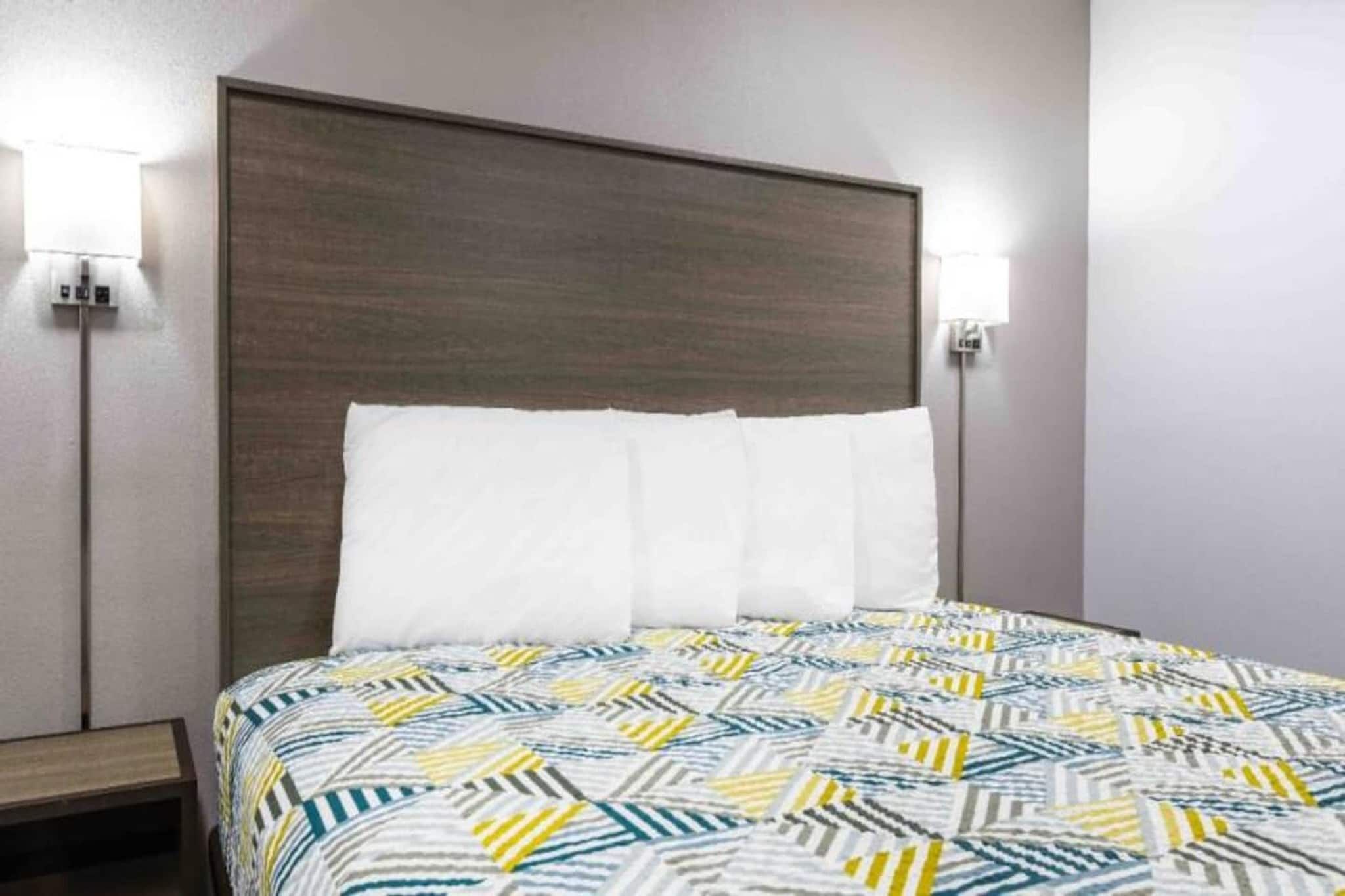 Ein Hotelzimmer mit einem Bett, einem Kopfteil, zwei Wandleuchten und einem Nachttisch.