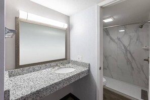 Ein Badezimmer mit Granitplatte, einem Spiegel, einer Dusche mit Marmorwänden und einer Toilette.
