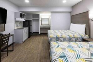 A compact hotel room with a kitchenette, a bed with patterned bedding, a desk, and a chair. - 2 Queen Beds | Smoking, Kitchen (Hickory)