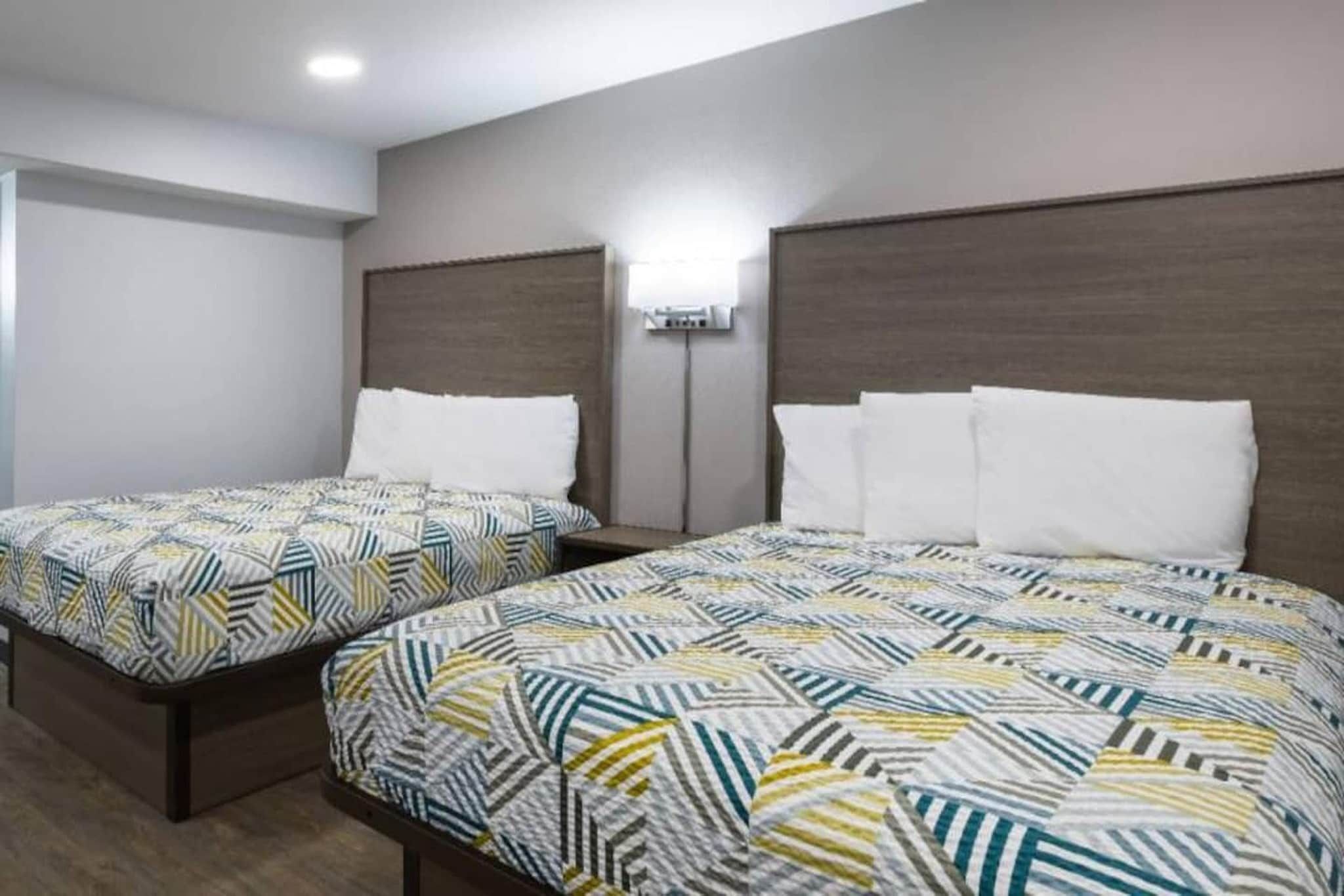 Une chambre d’hôtel avec deux lits, chacun agrémenté de draps à motifs, un climatiseur fixé au mur et un luminaire au plafond.