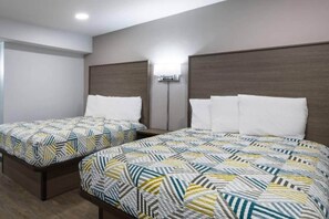 Een hotelkamer met twee bedden, elk voorzien van beddengoed met een patroon, een wandairconditioner en een plafondlamp.