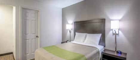 A hotel room with a bed, bedside tables, and a door.