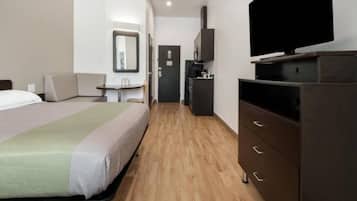 A hotel room with a bed, a television on a dresser, a small table with a chair, and a door leading to a bathroom.