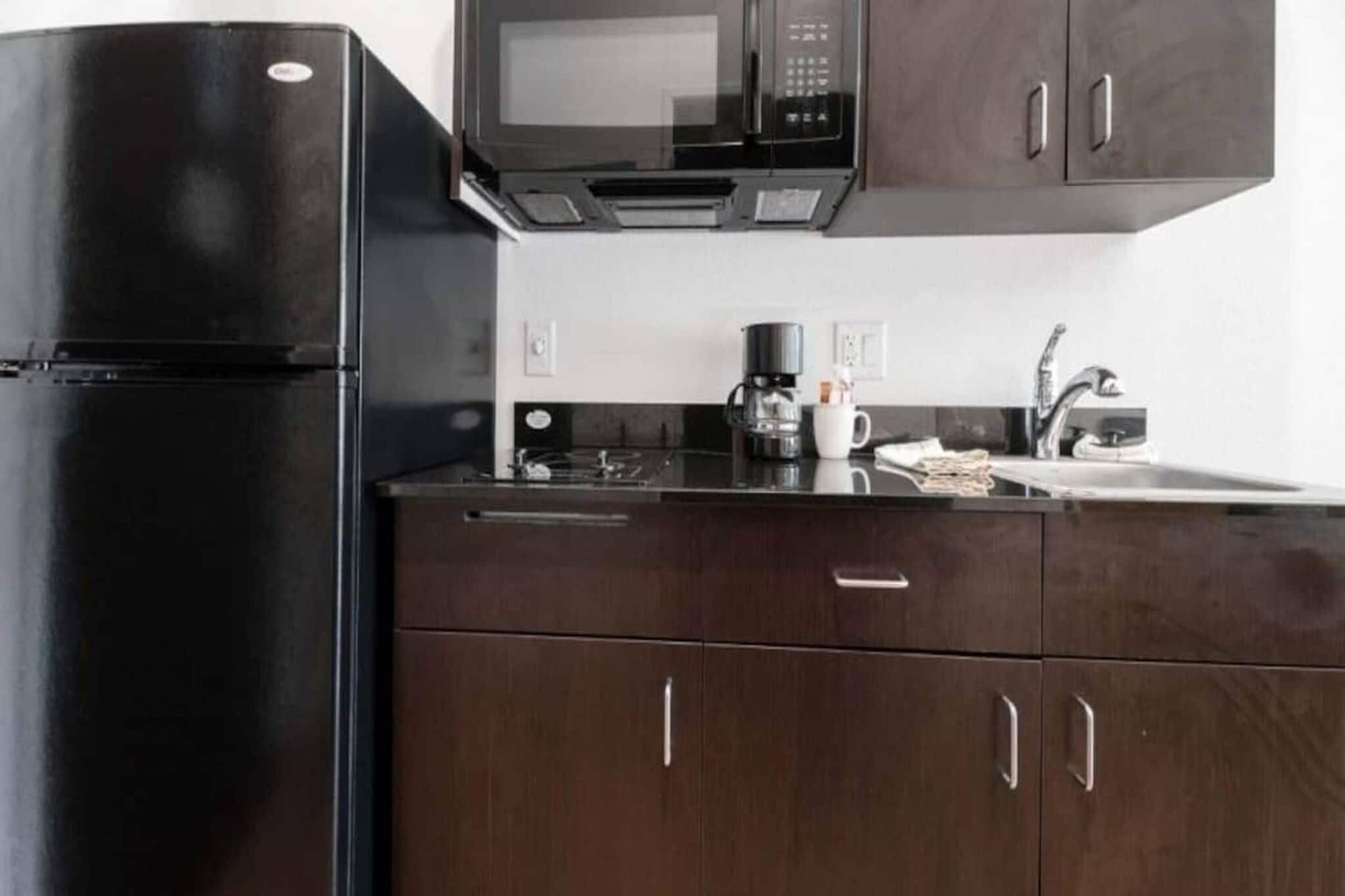 Una cocina con un refrigerador negro, un microondas, una cafetera y armarios de madera.