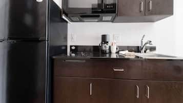 A kitchen with a black refrigerator, a microwave, a coffee maker, and wooden cabinets.