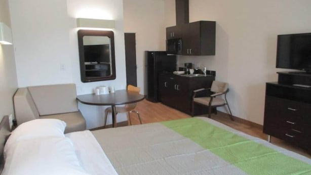 Een hotelkamer met een bed, een bureau, een stoel, een televisie en een kitchenette.