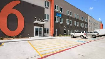 A modern building with a large '6' sign, a parking lot with marked spaces, and a few parked vehicles.