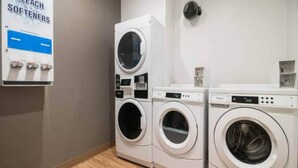 Een wasserette met gestapelde wasmachines en drogers, een bedieningspaneel en een bordje dat aangeeft dat er wasverzachter beschikbaar is.