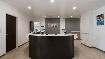 A reception desk with a curved black counter, two computer monitors, and a wall-mounted sign above.