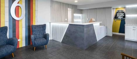 A reception area with a large number '6' on the wall, a reception desk, two blue armchairs, and a sign with a light bulb message.