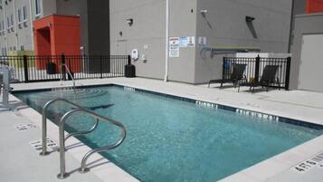 Una piscina con una escalera metálica, rodeada por una valla, y un flotador en la pared.