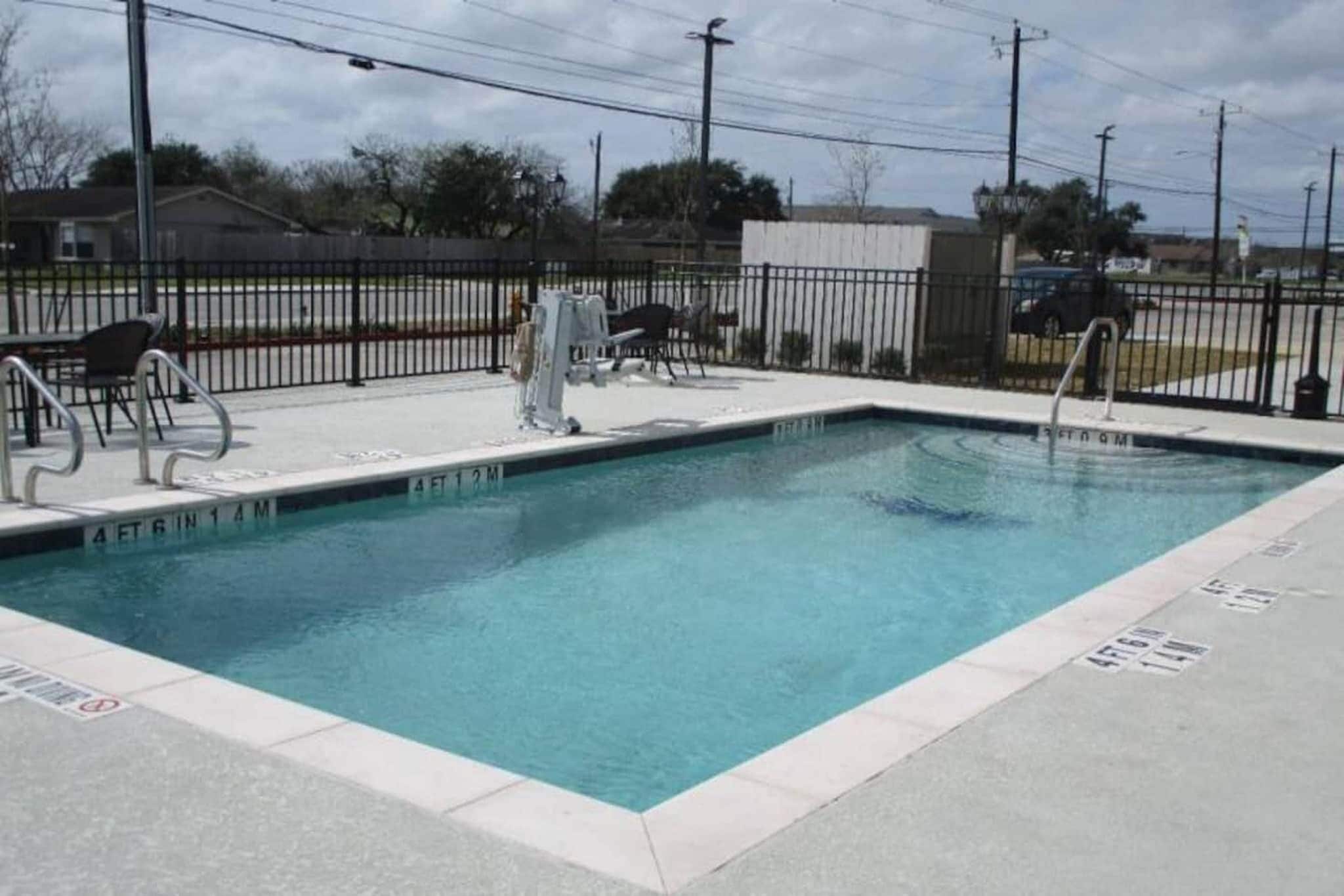 Una piscina rectangular con una escalera de metal en un lado, rodeada por una cerca de metal negro.