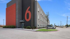 A building with a large red number '6' on its facade, a parking lot, and a single car parked in front. - 2 Queen Beds|Hearing Accessible,Kitchen (Corpus Christi TX)