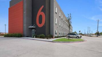Un edificio con un gran número 6 rojo en su fachada, un estacionamiento y un coche aparcado en la entrada.