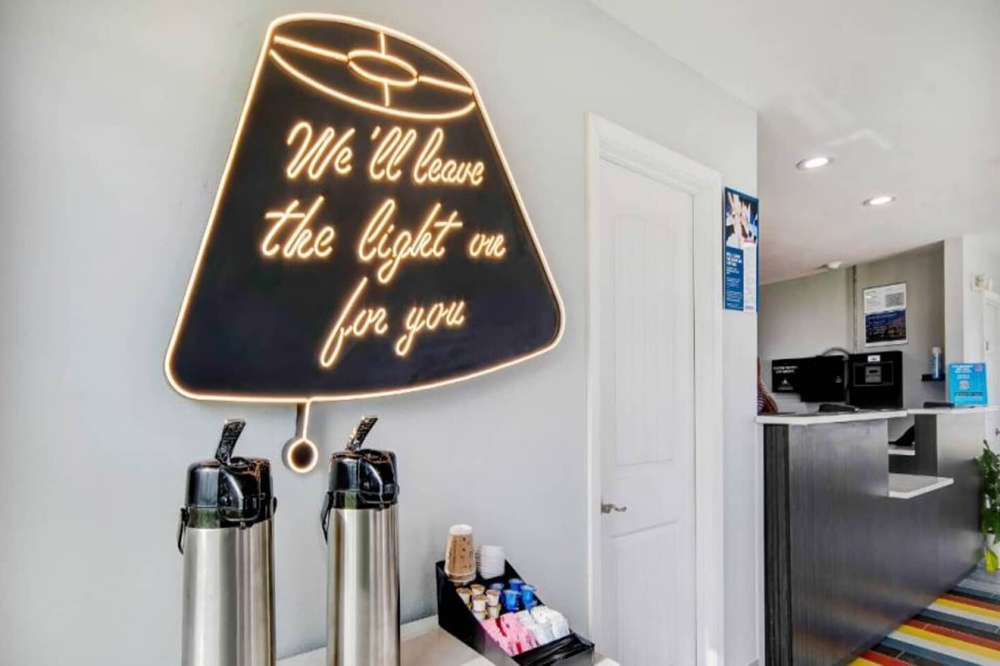 A neon sign with a message, a coffee machine, and a beverage dispenser.