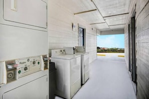 Een wasserette met industriƫle wasmachines en drogers, een bedieningspaneel en uitzicht op het buiten.
