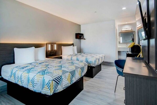 Quarto de hotel com duas camas, uma escrivaninha, uma cadeira e um espelho.