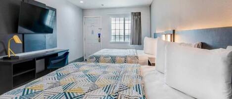 A hotel room with a large bed, a desk with a chair, a TV mounted on the wall, and a window with curtains.