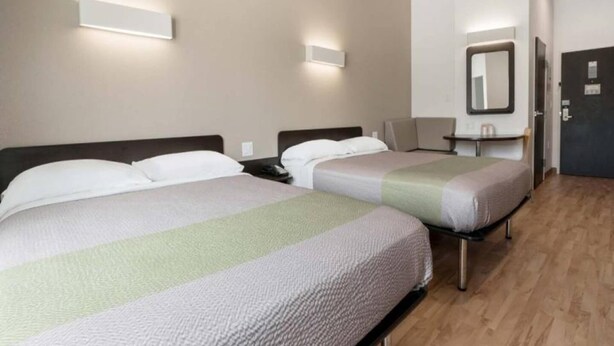 Une chambre d’hôtel avec deux lits, une table de chevet, une chaise, un bureau et un miroir au mur.