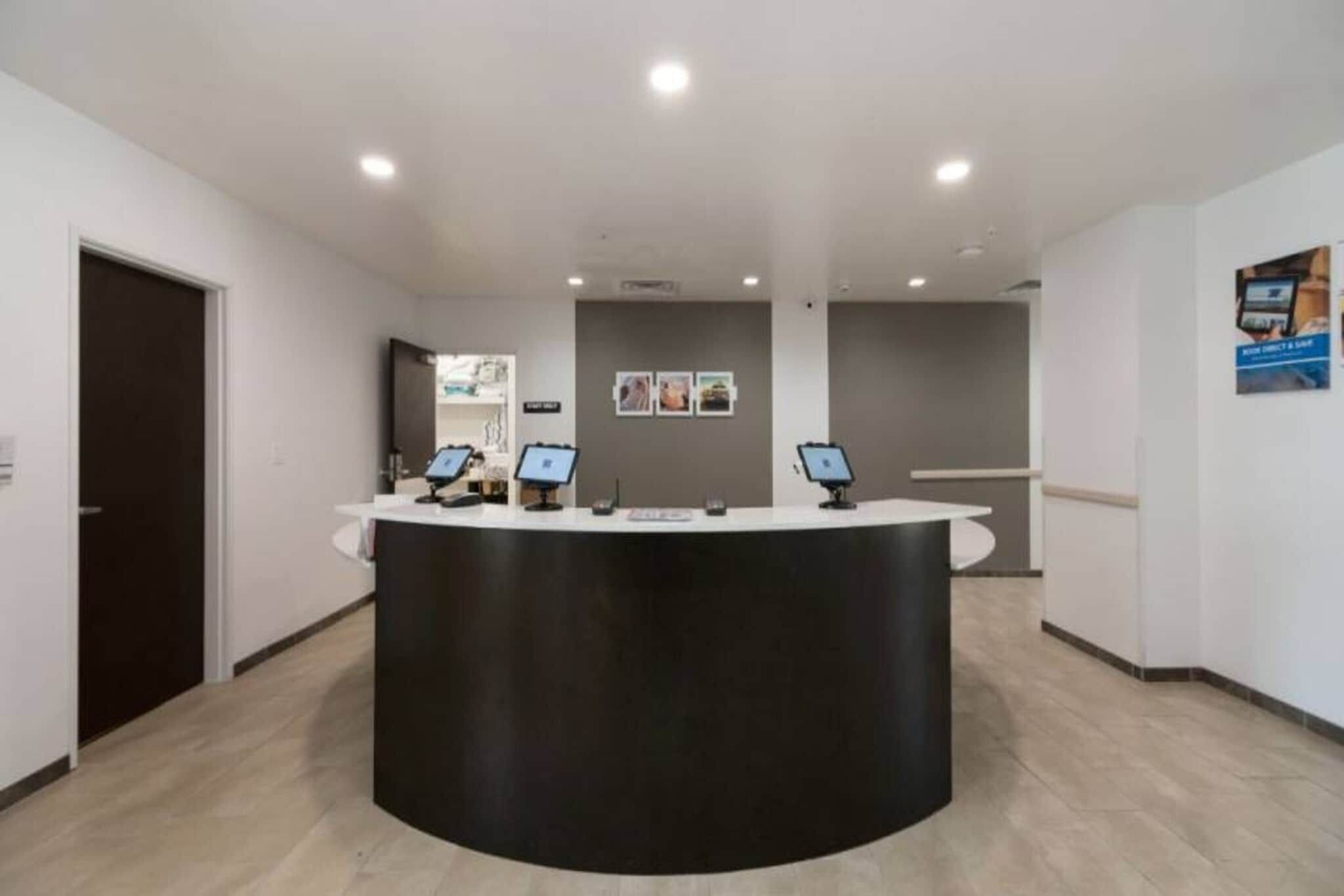 Un área de recepción con una barra negra curva, dos monitores de computadora y una puerta a la izquierda.