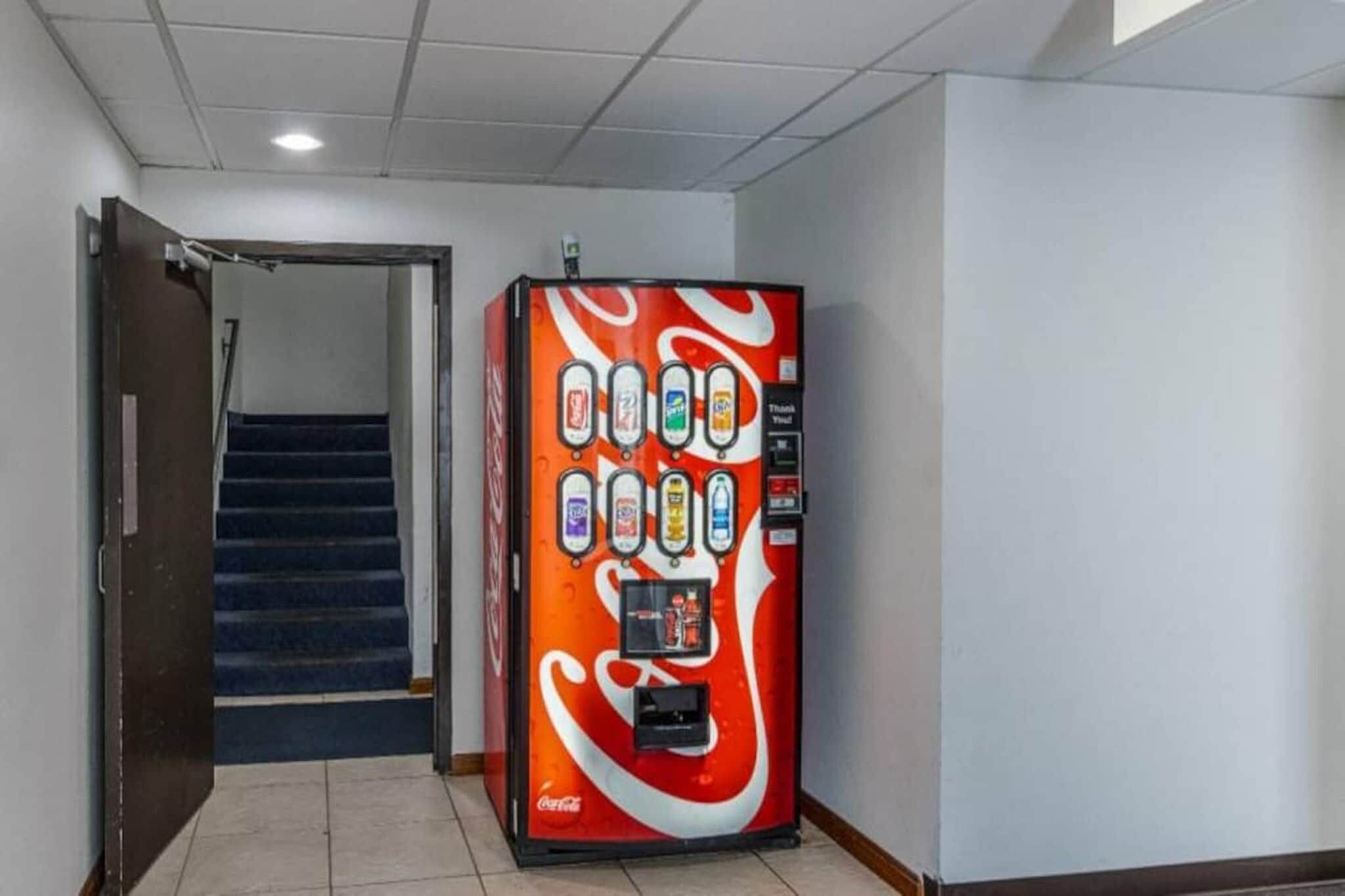 Una máquina expendedora con el logotipo de Coca-Cola, ubicada en un pasillo con una escalera.
