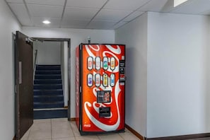 A vending machine with a Coca-Cola logo, located in a hallway with a staircase.