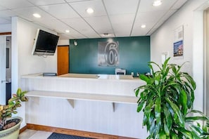 A reception desk with a digital screen, a teal accent wall, and a large green plant.