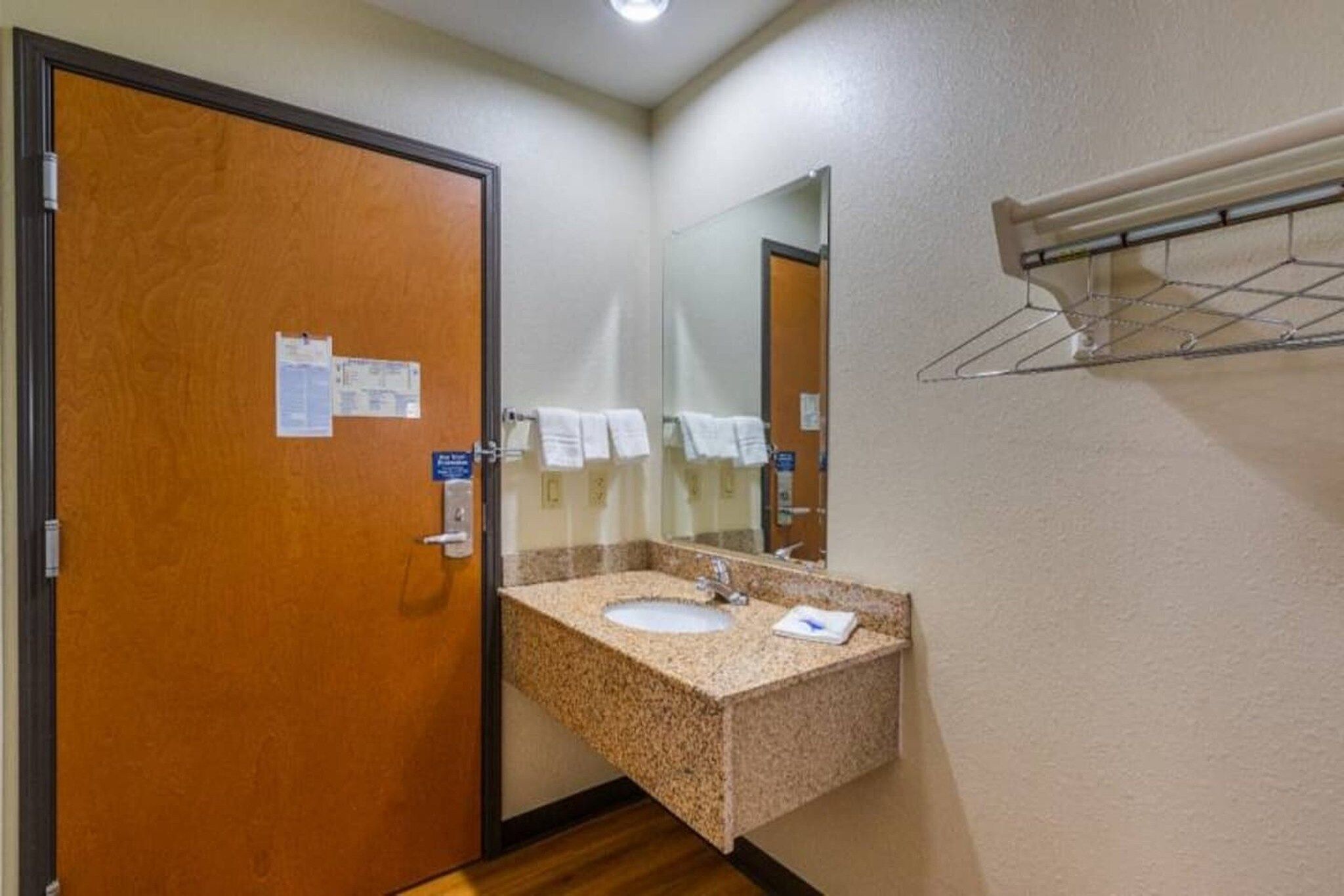 A hotel bathroom with a wooden door, a granite sink, a mirror, and a towel rack.
