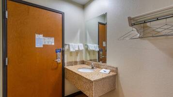 A hotel bathroom with a wooden door, a granite sink, a mirror, and a towel rack.